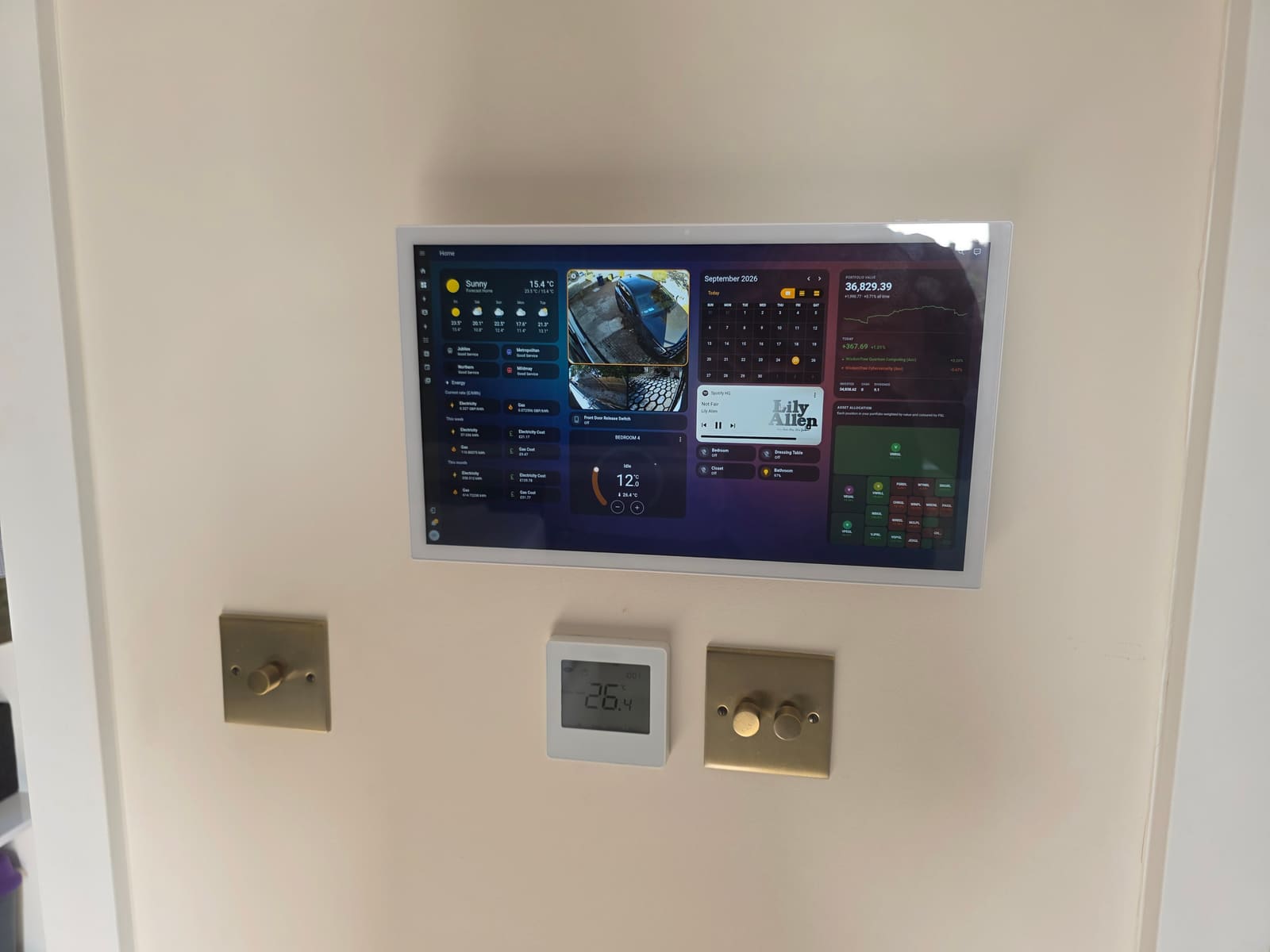 15.6-inch Android PoE tablet mounted on a hallway wall above two brass dimmer switches, showing a Home Assistant dashboard
