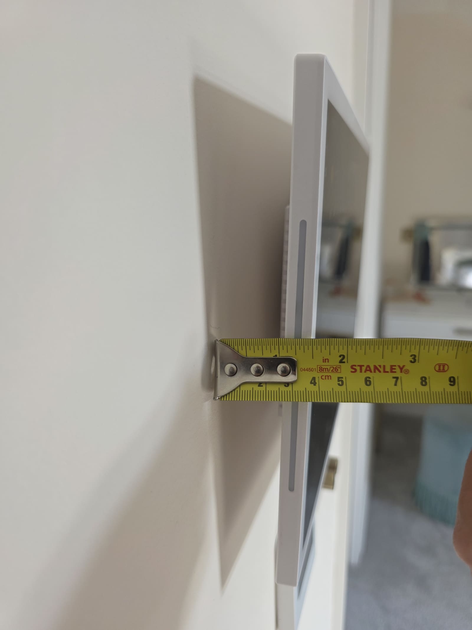 Tape measure held from the wall to the front edge of a white wall tablet frame showing about 4cm projection