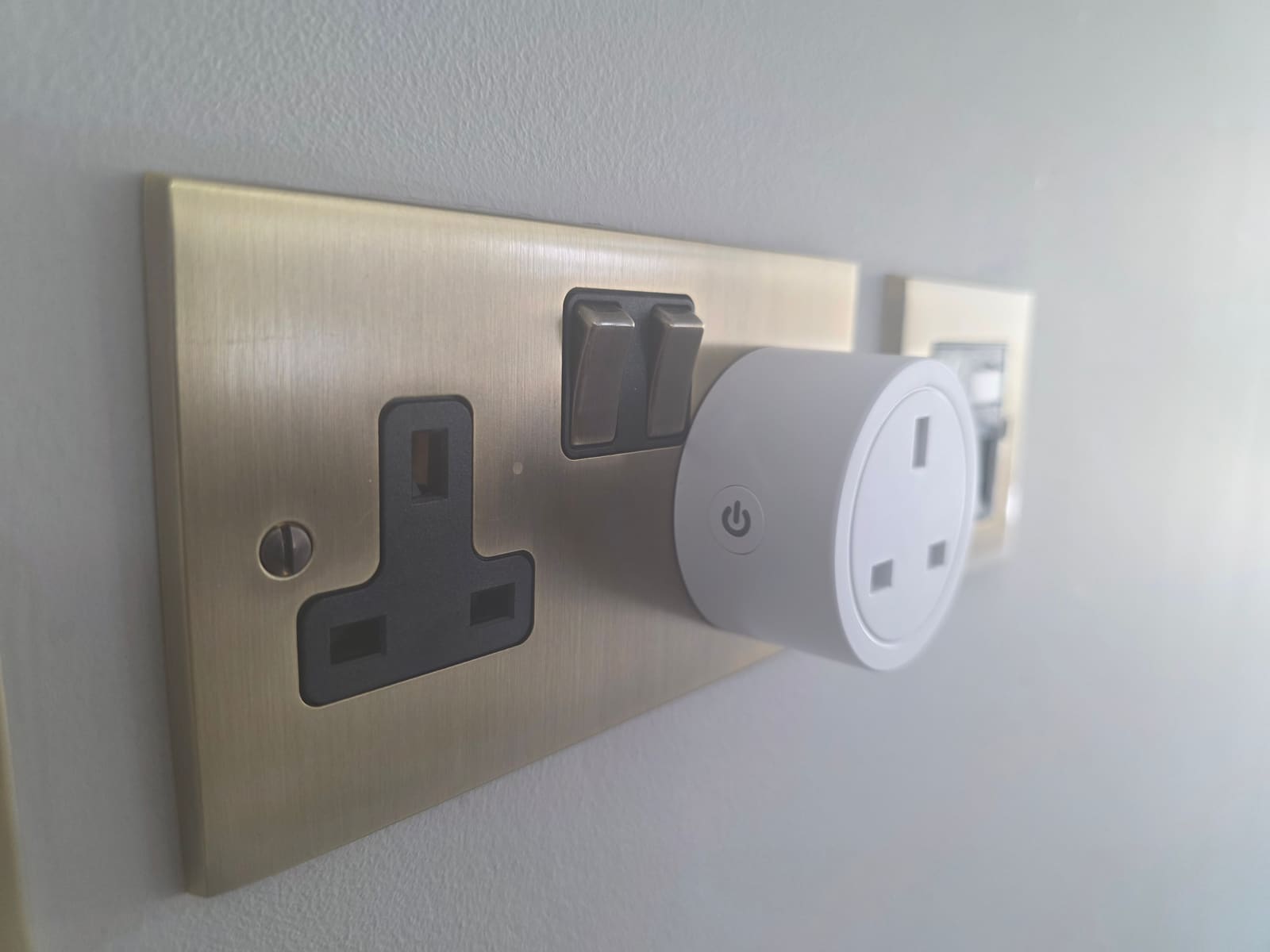 IoTorero ESP32-C3 smart plug fitted into a UK double wall socket next to a light switch