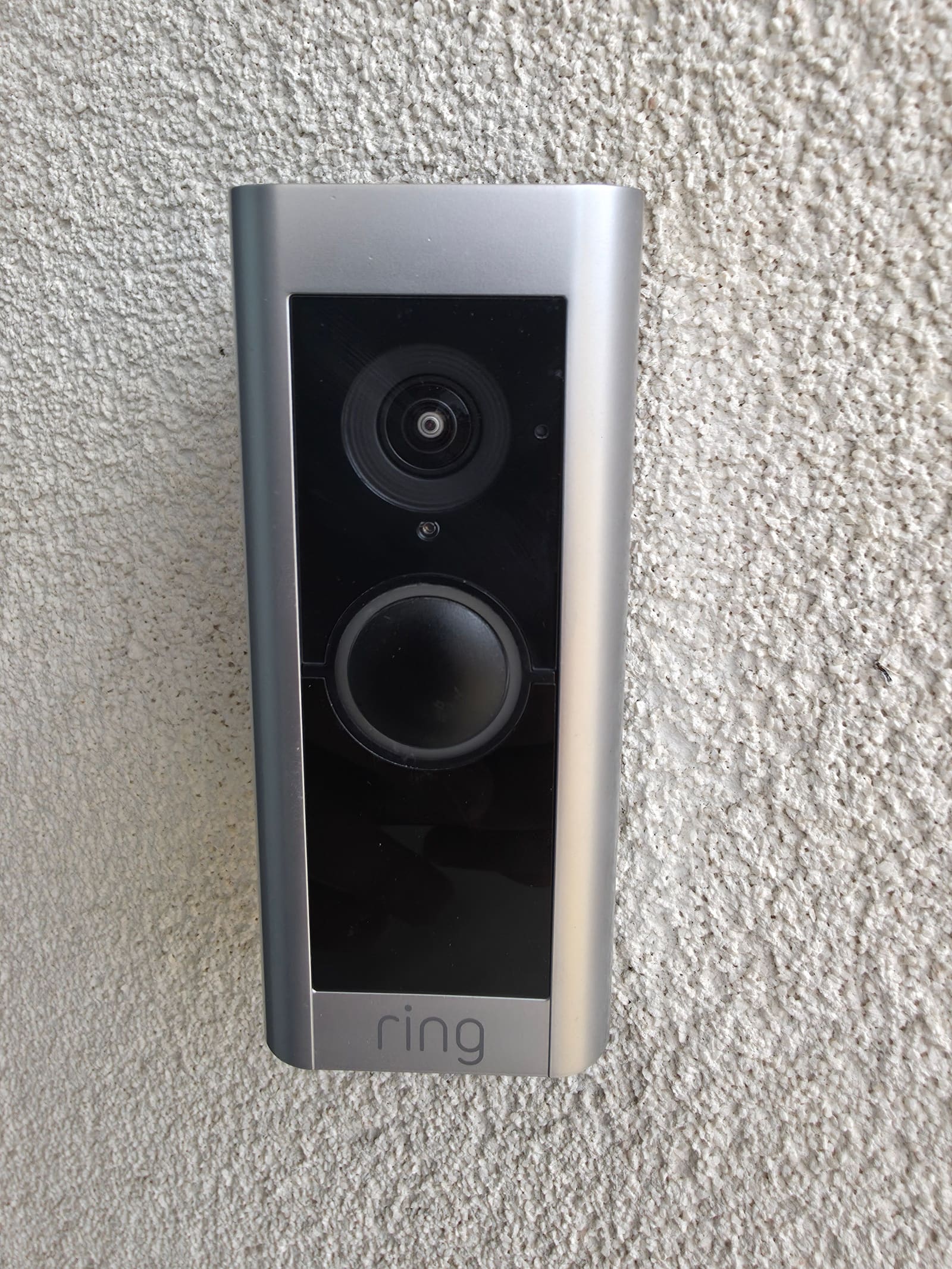 Silver hardwired Ring doorbell mounted on a pebbledash wall before being replaced