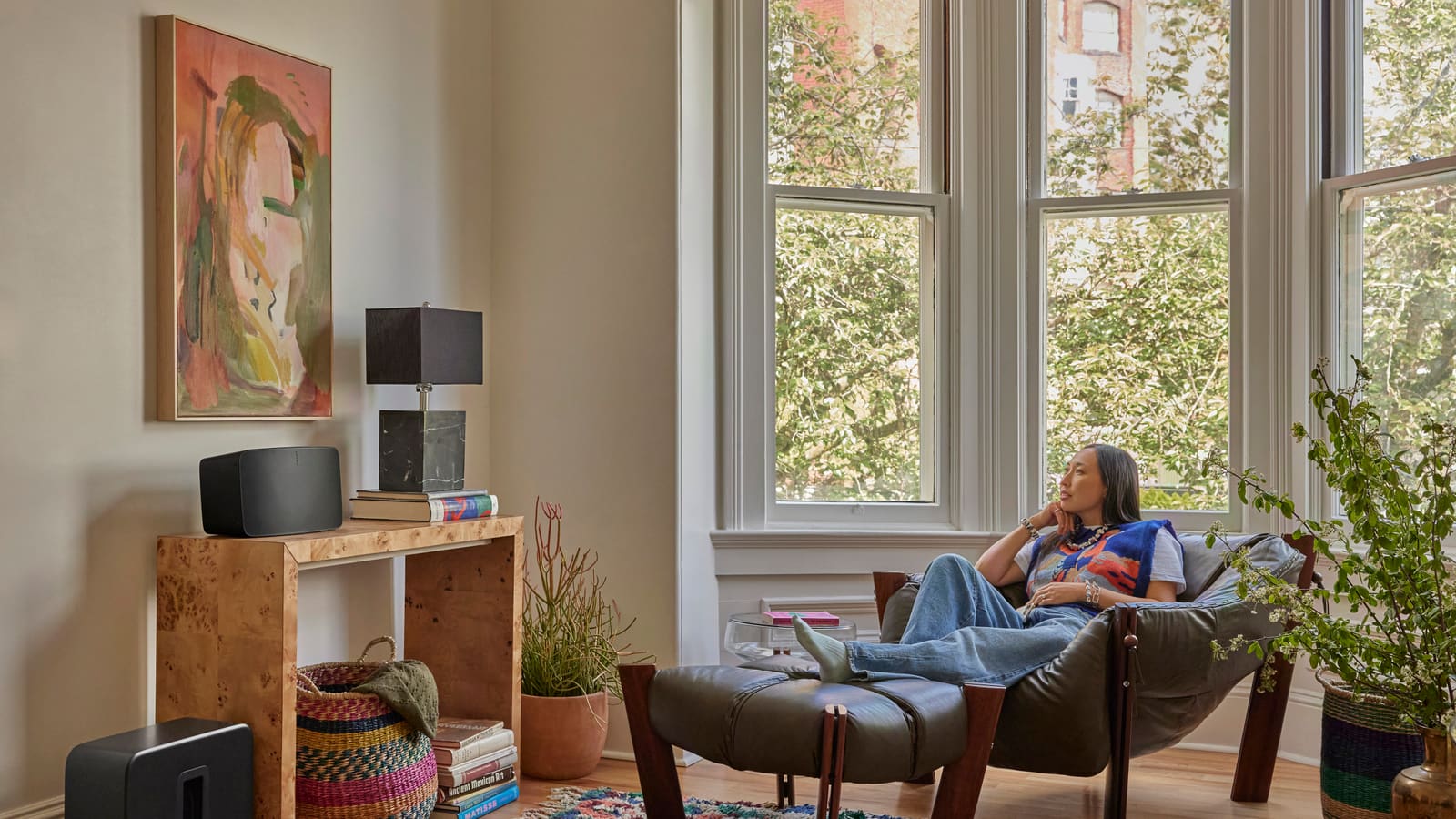 Woman relaxing in an armchair in a bright living room with a Sonos Five speaker and Sub 4 subwoofer