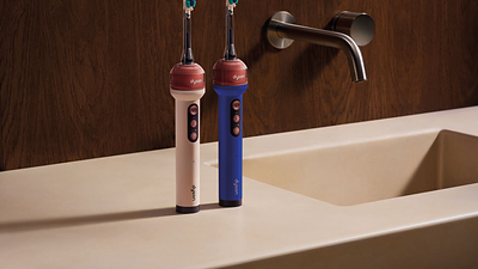 Two Dyson CameraJet toothbrushes, pink and blue, standing upright on a bathroom counter.