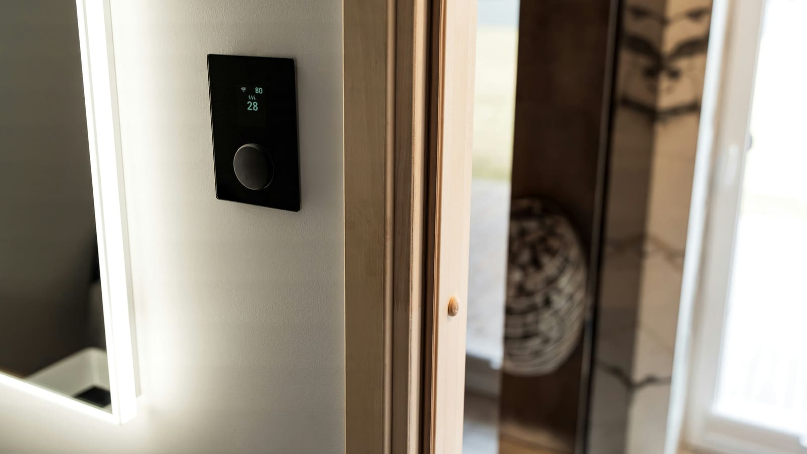 Modern black wall-mounted control panel with a small digital display beside a door in a bright interior