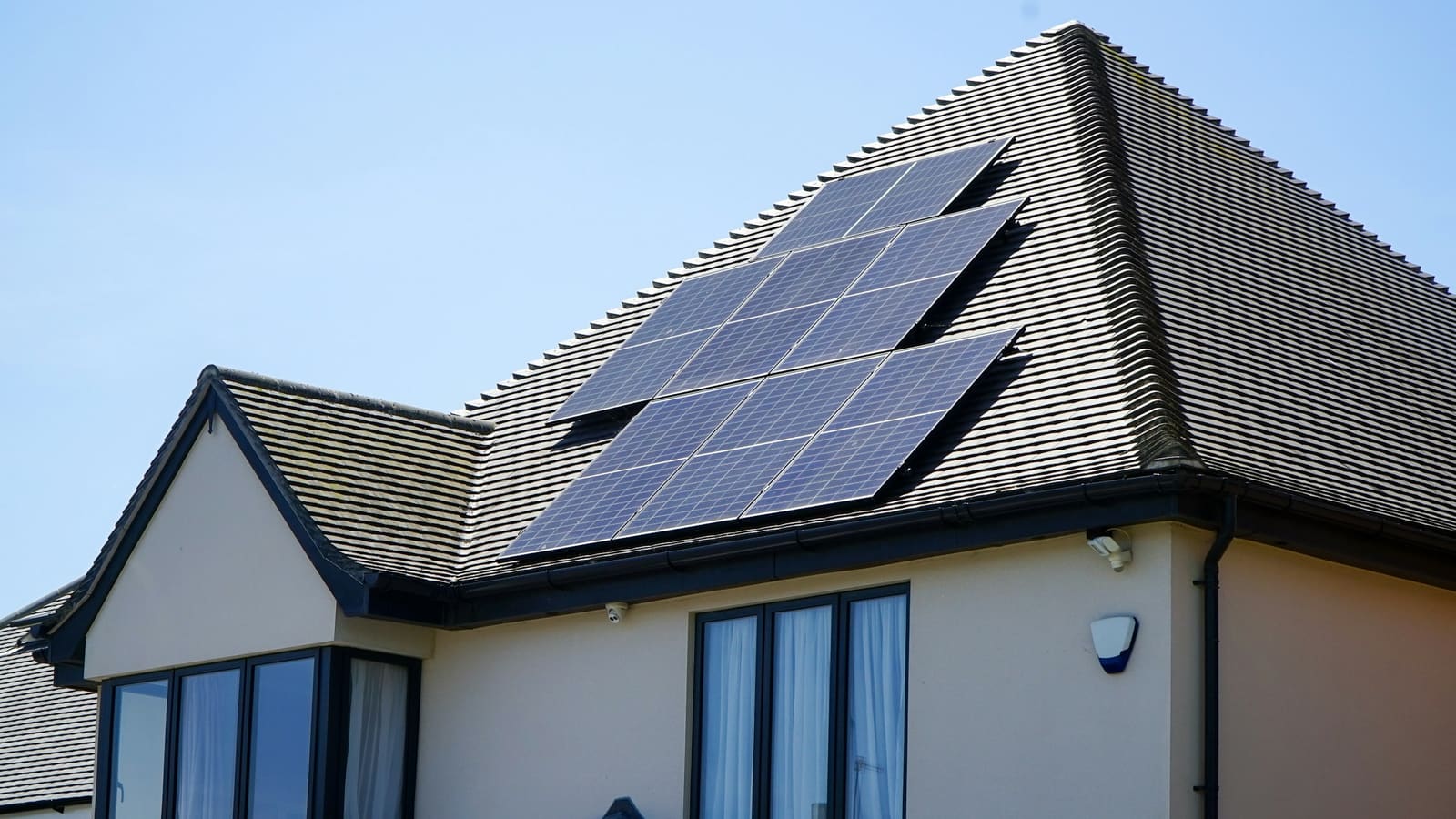 Rows of dark solar panels on a tiled house roof beneath a clear blue sky