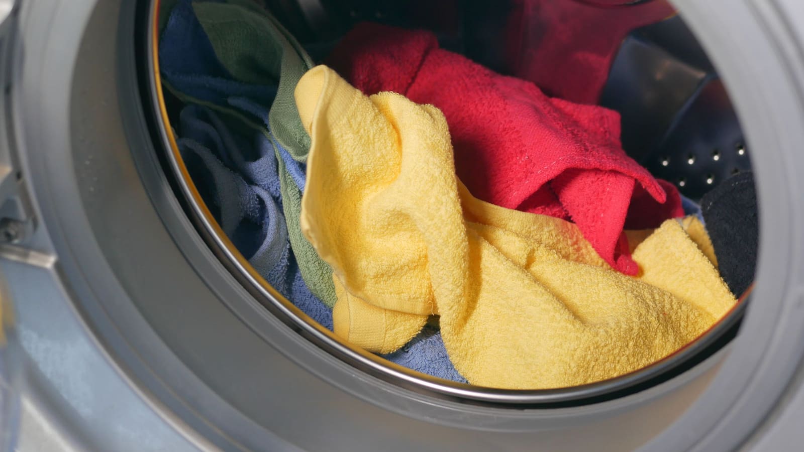Close-up of colourful towels inside the open drum of a front-loading washing machine